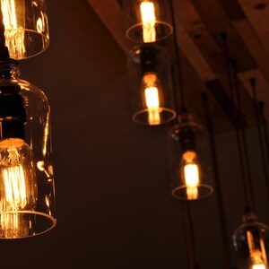 May include: A group of Edison bulb light fixtures hanging from a wooden ceiling. The bulbs are encased in clear glass bottles.