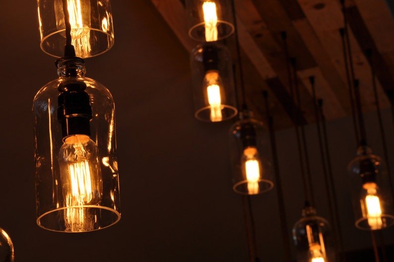 May include: A group of Edison bulb light fixtures hanging from a wooden ceiling. The bulbs are encased in clear glass bottles.