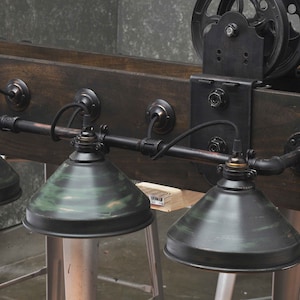 May include: A rustic industrial style light fixture with four black and green metal shades. The fixture is mounted on a wooden beam with a black metal pulley and bracket.