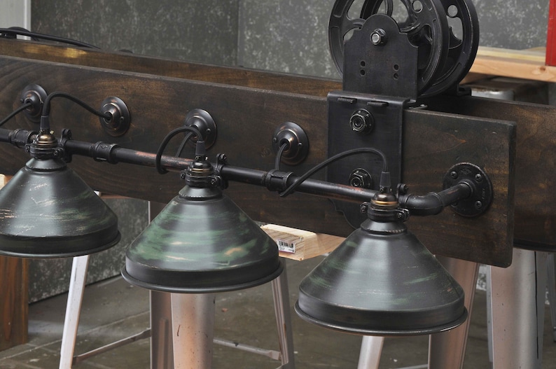 May include: A rustic industrial style light fixture with four black and green metal shades. The fixture is mounted on a wooden beam with a black metal pulley and bracket.