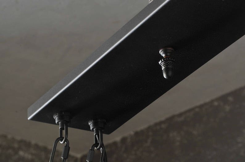 Puede incluir: Luminaria de techo de metal negro con tres cables colgantes y un remate decorativo en forma de bellota.