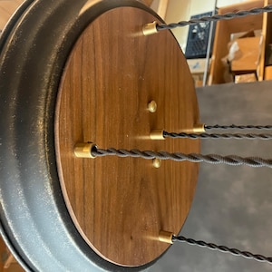 May include: A round wooden ceiling fixture with a black metal rim. The fixture has five brass wire connectors and black braided cords hanging from it.