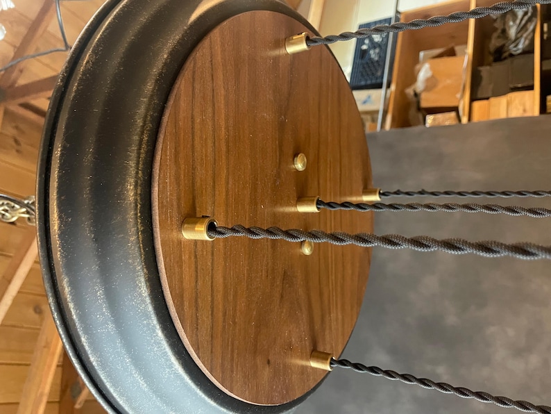 May include: A round wooden ceiling fixture with a black metal rim. The fixture has five brass wire connectors and black braided cords hanging from it.