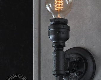 May include: Black industrial style wall sconce with a round black metal base and a single light bulb. The light bulb is a vintage style filament bulb with a spiral filament.