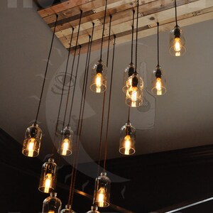 May include: A rustic chandelier made from reclaimed wood with 12 glass bottle light fixtures. The chandelier is hanging from the ceiling and the lights are turned on, casting a warm glow.