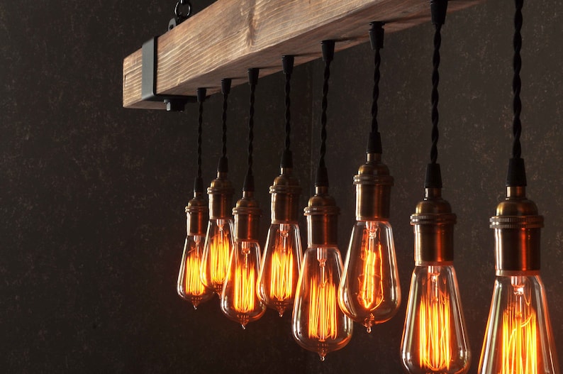 Op de afbeelding: Een rustieke houten balk-kroonluchter met 10 blootliggende gloeilampen. De lampen hangen aan zwarte snoeren en hebben een warme, amberkleurige gloed.