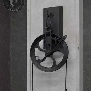 Puede incluir: L&aacute;mpara colgante de estilo industrial negro con una polea y una pantalla de botella de vidrio transparente. La luz est&aacute; montada en una placa de metal negro y tiene un cable negro. La luz est&aacute; etiquetada "Moonshine Lamp Co."