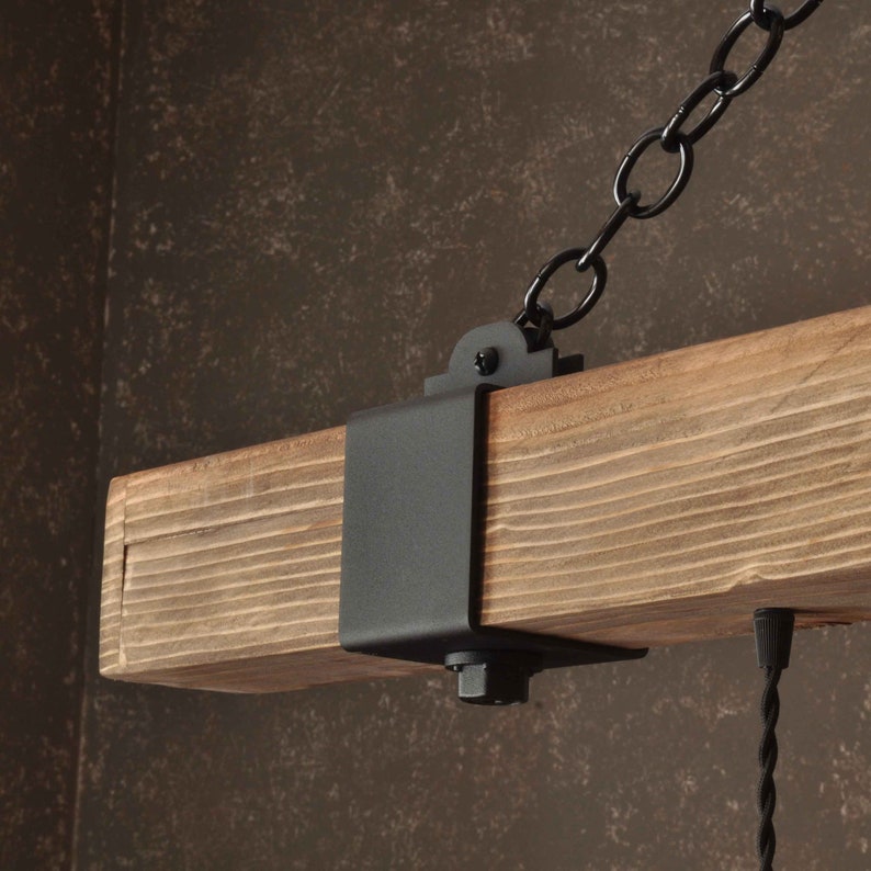 Op de afbeelding: Een rustieke houten balk met een zwarte metalen beugel en een ketting die eraan hangt. De balk is gemaakt van natuurlijk hout met een ruwe textuur. De beugel is met schroeven aan de balk bevestigd en heeft een eenvoudig ontwerp. De ketting is gemaakt van metalen schakels en is verbonden met de beugel. De balk is een decoratief element dat in verschillende omgevingen kan worden gebruikt.