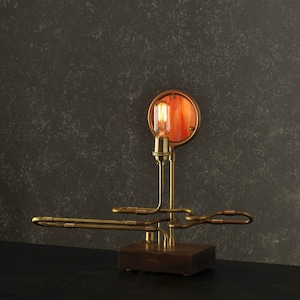 May include: A brass steampunk-style table lamp with a round, orange-tinted glass shade and a wooden base.