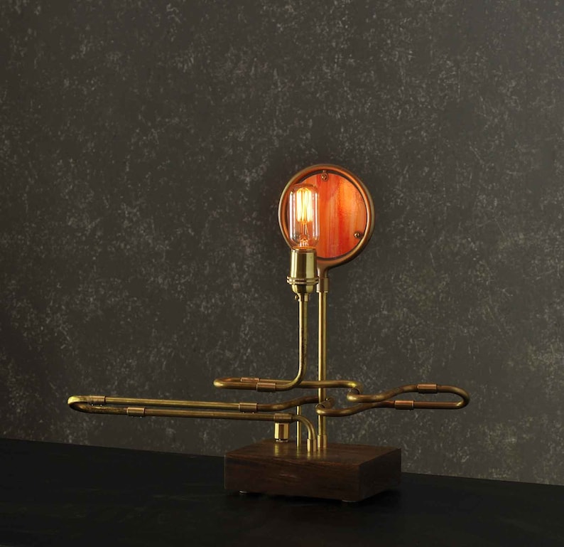 May include: A brass steampunk-style table lamp with a round, orange-tinted glass shade and a wooden base.