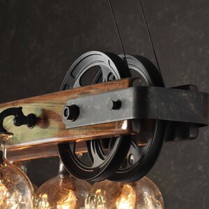 Puede incluir: Una l&aacute;mpara de ara&ntilde;a de madera r&uacute;stica con poleas de metal negro y globos de vidrio. La l&aacute;mpara de ara&ntilde;a tiene un acabado de madera desgastada y es perfecta para una casa de estilo r&uacute;stico o industrial.