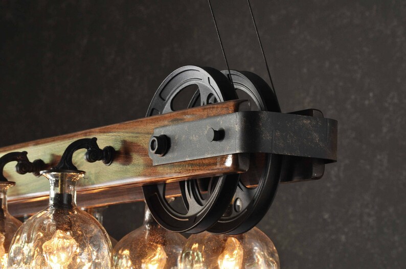 Puede incluir: Una l&aacute;mpara de ara&ntilde;a de madera r&uacute;stica con poleas de metal negro y globos de vidrio. La l&aacute;mpara de ara&ntilde;a tiene un acabado de madera desgastada y es perfecta para una casa de estilo r&uacute;stico o industrial.