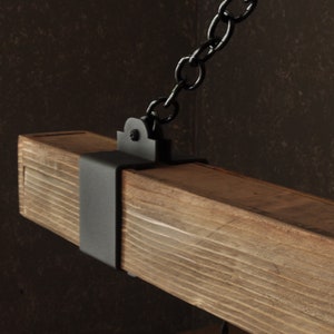 Op de afbeelding: Een rustieke houten balk met een zwarte metalen beugel en een ketting die eraan hangt. De balk is gemaakt van natuurlijk hout met een ruwe textuur en een donkerbruine kleur. De beugel is met schroeven aan de balk bevestigd en heeft een eenvoudig ontwerp. De ketting is gemaakt van metalen schakels en is verbonden met de beugel. De balk is een decoratief element dat in verschillende omgevingen kan worden gebruikt, zoals een huis, kantoor of restaurant.