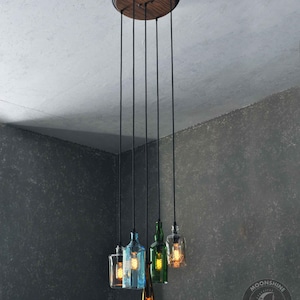 May include: A five-light pendant light fixture with a wooden canopy and black cords. The light bulbs are encased in glass bottles of various colors, including green, blue, and clear.