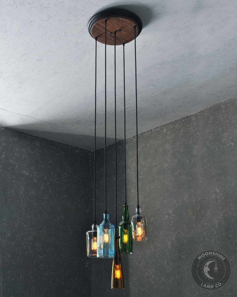 May include: A five-light pendant light fixture with a wooden canopy and black cords. The light bulbs are encased in glass bottles of various colors, including green, blue, and clear.