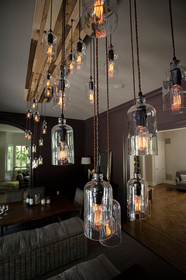 May include: A rustic chandelier with multiple glass bulbs hanging from a wooden beam. The bulbs are lit and cast a warm glow. The chandelier is suspended from the ceiling with brown cords.