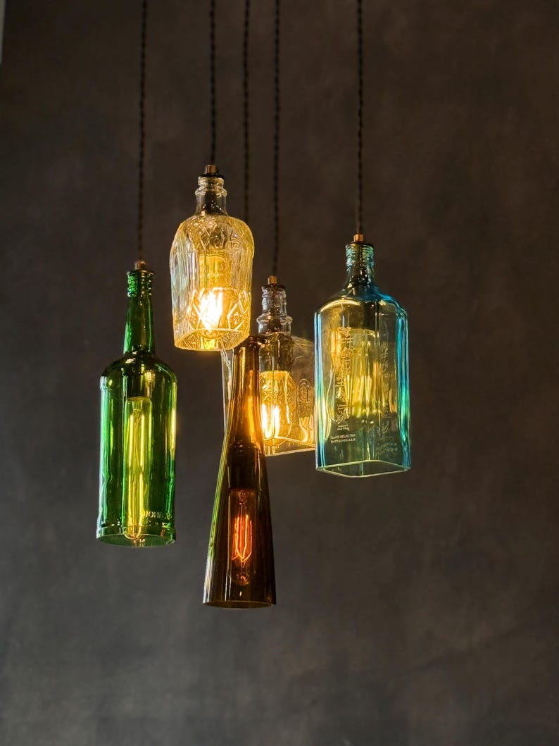May include: Five glass bottles with light bulbs inside, hanging from the ceiling. The bottles are different shapes and sizes, and they are all lit up. The bottles are green, blue, and clear.