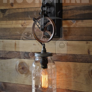 May include: A rustic wall-mounted light fixture with a copper pulley and a mason jar glass shade. The light fixture is mounted on a wooden wall with the text "Moonshine Lane Co." visible.