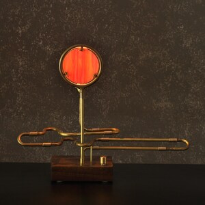 May include: A brass table lamp with a red glass shade. The lamp has a unique design with a curved arm and a round base.