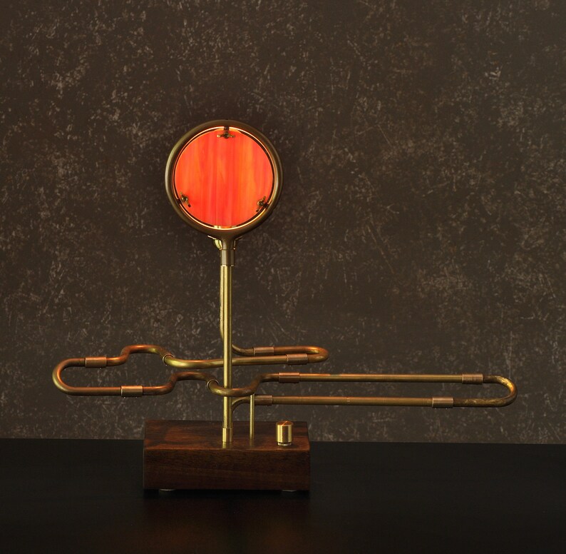 May include: A brass table lamp with a red glass shade. The lamp has a unique design with a curved arm and a round base.