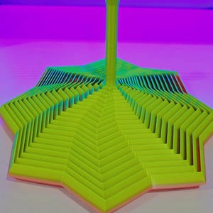 May include: A lime green, star-shaped, multi-layered object with a central vertical post. The structure features concentric, stepped geometric rings that decrease in size toward the center, creating a tiered, three-dimensional appearance.
