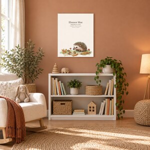 Storybook hedgehog canvas in a nursery on a terracotta wall above a white bookshelf, showing sample name Eleanor Mae and birth details.