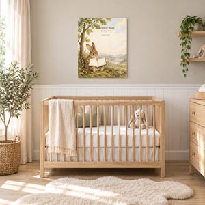 Storybook rabbit canvas in a nursery on a greige wall above a wooden crib and white wainscoting, showing sample name Eleanor Mae and birth details.