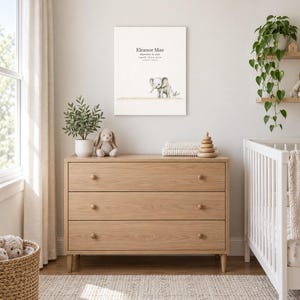 Baby elephant canvas in a nursery above a light oak dresser beside a white crib, showing sample name Eleanor Mae and birth details.