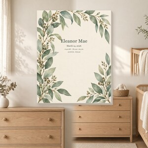 May include: A rectangular wall art print featuring a watercolor illustration of green eucalyptus leaves and berries framing the text: Eleanor Mae, March 14, 2026, 6:42 AM, 7 lb 4 oz, 20.5 in, Austin, Texas, set against a cream-colored background.