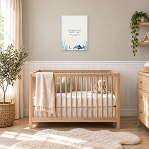 Ocean birth stats sign in a nursery on a greige wall above a wooden crib and white wainscoting, showing sample name Eleanor Mae and birth details.