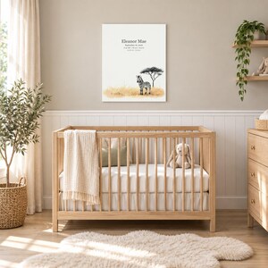 Baby zebra canvas in a nursery on a greige wall above a wooden crib and white wainscoting, showing sample name Eleanor Mae and birth details.