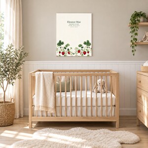 Strawberry canvas in a nursery on a greige wall above a wooden crib and white wainscoting, showing sample name Eleanor Mae and birth details.