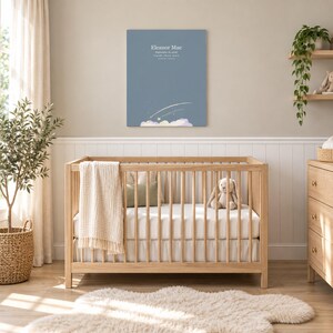 Shooting star canvas in a nursery on a greige wall above a wooden crib and white wainscoting, showing sample name Eleanor Mae and birth details.
