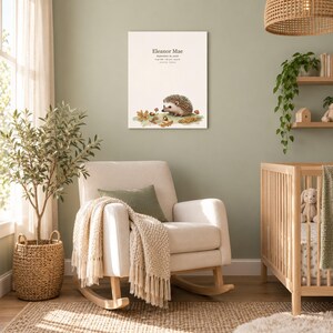 Storybook hedgehog canvas in a nursery on a sage green wall above a cream rocking chair, showing sample name Eleanor Mae and birth details.