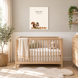 Little squirrel canvas in a nursery on a greige wall above a wooden crib and white wainscoting, showing sample name Eleanor Mae and birth details.