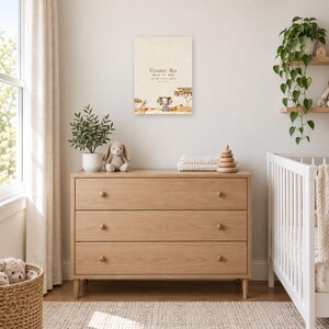 Safari birth stats sign in a nursery above a light oak dresser beside a white crib, showing sample name Eleanor Mae and birth details.