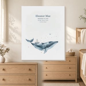 May include: A white rectangular wall art print featuring a watercolor blue whale with a small sailboat on its back. The text reads Eleanor Mae, September 16, 2026, 6:42 AM, 7 lb 4 oz, 20.5 in, and Austin, Texas, with small gold stars and a crescent moon.