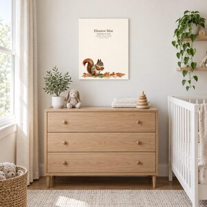Little squirrel canvas in a nursery above a light oak dresser beside a white crib, showing sample name Eleanor Mae and birth details.