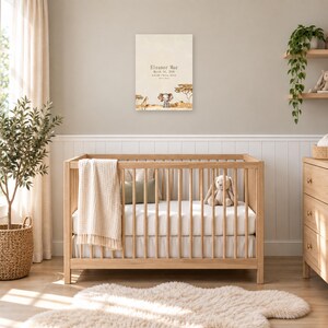 Safari birth stats sign in a nursery on a greige wall above a wooden crib and white wainscoting, showing sample name Eleanor Mae and birth details.