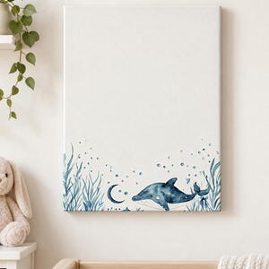 Wrapped ocean nursery canvas with a blue watercolor whale, crescent moon, bubbles and sea plants displayed above a crib.