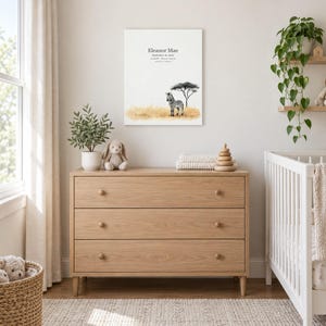 Baby zebra canvas in a nursery above a light oak dresser beside a white crib, showing sample name Eleanor Mae and birth details.