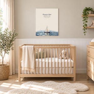 Sailboat canvas in a nursery on a greige wall above a wooden crib and white wainscoting, showing sample name Eleanor Mae and birth details.