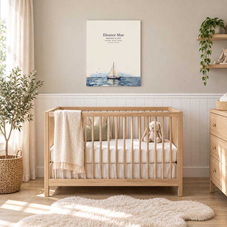 Sailboat canvas in a nursery on a greige wall above a wooden crib and white wainscoting, showing sample name Eleanor Mae and birth details.