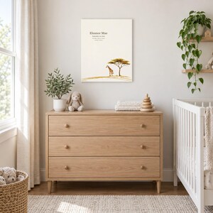 Safari giraffe canvas in a nursery above a light oak dresser beside a white crib, showing sample name Eleanor Mae and birth details.