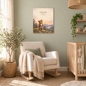Woodland bear canvas in a nursery on a sage green wall above a cream rocking chair, showing sample name Eleanor Mae and birth details.