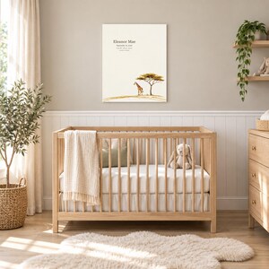 Safari giraffe canvas in a nursery on a greige wall above a wooden crib and white wainscoting, showing sample name Eleanor Mae and birth details.