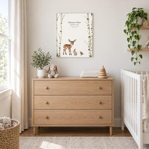 Meadow fawn canvas in a nursery above a light oak dresser beside a white crib, showing sample name Eleanor Mae and birth details.