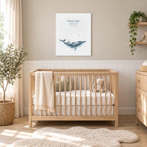 Moonlit whale canvas in a nursery on a greige wall above a wooden crib and white wainscoting, showing sample name Eleanor Mae and birth details.