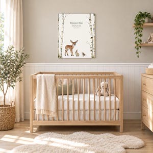 Meadow fawn canvas in a nursery on a greige wall above a wooden crib and white wainscoting, showing sample name Eleanor Mae and birth details.