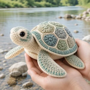May include: A crochet turtle toy featuring a cream-colored head and limbs with a multi-toned shell composed of hexagonal patches in shades of sage green, dusty blue, and beige. The turtle has large, round, black plastic eyes and a textured surface.